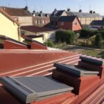 Trois costières bac acier JUMO posées sur un bac acier coloris rouge (RAL 8012).